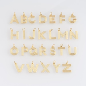 May include: Gold-colored alphabet letter charms, each with a loop for attaching to a necklace or bracelet. The letters are in a sans-serif font with a striped design. The letters A through Z are displayed.