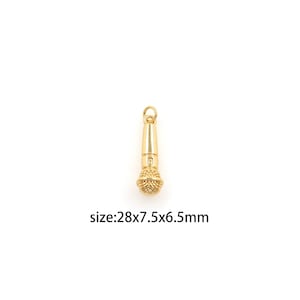 May include: A gold-colored microphone charm with a detailed, textured head and a smooth, cylindrical body. The charm includes a small loop at the top for attachment. The text on the image reads: size:28x7.5x6.5mm.