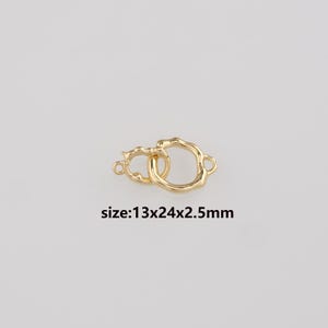 Könnte beinhalten: Ein goldfarbener Verschluss mit zwei ineinandergreifenden Ringen und einem strukturierten, organischen Design. Der Text "size:13x24x2.5mm" ist darunter aufgedruckt. Der Verschluss misst 1,3 cm x 2,4 cm x 0,25 cm und eignet sich für Schmuck.