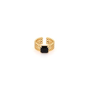 May include: A gold ring with a black square-shaped gemstone set in the center. The ring band is made of a delicate, openwork design.