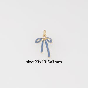 May include: A gold-toned metal charm shaped like a bow with blue enamel detailing and a small clear stone at the center. The charm features a loop at the top for attachment. The text size:23x13.5x3mm is printed below the bow charm.