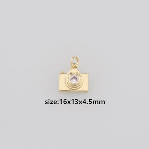 Peut inclure: Breloque en forme d'appareil photo doré avec un strass transparent au centre. Le breloque mesure 16x13x4,5 mm.