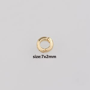 Op de afbeelding: Een goudkleurige, ronde sieradensluiting met een scharnierende opening. De sluiting is 7 mm bij 2 mm groot, zoals aangegeven door de tekst op de afbeelding. De sluiting is ontworpen om sieraden te bevestigen.
