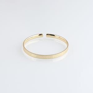 Op de afbeelding: Een gouden armband met een getextureerd oppervlak.