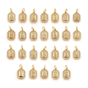 Puede incluir: Un conjunto de 26 colgantes de tono dorado, cada uno con una letra diferente del alfabeto, adornados con piedras de circonita cúbica transparentes. Los colgantes están diseñados en forma rectangular con un borde biselado.