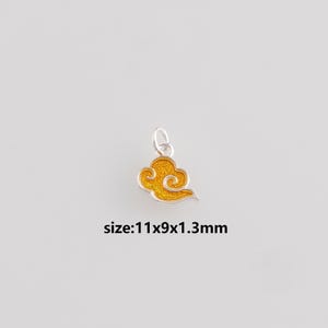 Może przedstawiać: Srebrny urok w kształcie chmury z jasnożółtym środkiem. Urok ma wymiary 1,1 cm x 0,9 cm x 1,3 mm. Wzór chmury ma wirujący wzór i małą pętlę na górze.