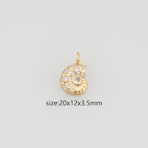 May include: A gold-toned nautilus shell pendant featuring embedded clear crystals and a small top loop for attachment. The pendant measures 20x12x3.5mm as indicated by the text printed below the object on the plain light background.