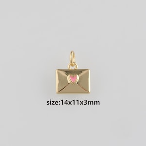 May include: A gold-coloured pendant shaped like an envelope, featuring a pink heart in the centre. The pendant measures 14x11x3mm. A bail is attached to the top. The background is a plain light grey.