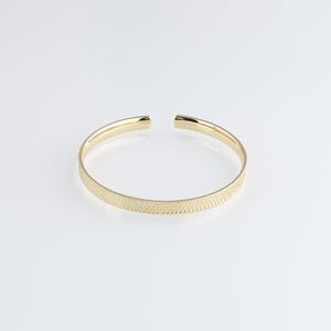 May include: A gold bangle bracelet with a textured surface.