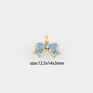 Könnte beinhalten: Ein goldfarbener Schleifenanhänger mit hellblauer Emaille und einer kleinen Schlaufe zum Aufhängen. Die Schleife misst 12,5 x 14 x 3 mm. Der Text "size:12.5x14x3mm" befindet sich darunter.