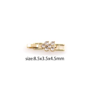 May include: Gold-toned metal connector with clear crystal embellishments in a flower shape. The connector measures 8.5 x 3.5 x 4.5 mm.