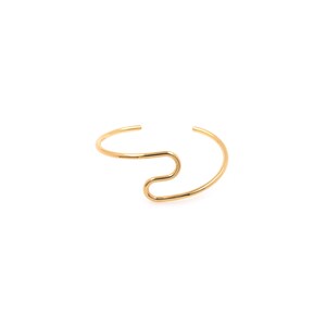 May include: A gold-toned metal bangle bracelet with a unique, abstract design. The bracelet is open and has a simple, minimalist style.