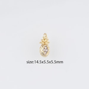May include: A gold-coloured pineapple charm with a textured surface and a loop for attaching to a chain or bracelet. The charm features a cluster of small, clear stones. The text "size:14.5x5.5x5.5mm" is visible.