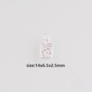 Puede incluir: Un pequeño colgante plateado con un diseño rectangular texturizado. Tiene un lazo para una cadena. Mide 1,4 cm x 0,65 cm x 0,25 cm. El texto "size:14x6.5x2.5mm" es visible debajo.
