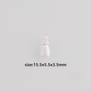 Puede incluir: Un pequeño dije de piña plateada con una superficie texturizada y un lazo para sujetarlo a una cadena o pulsera. El dije mide aproximadamente 1,6 x 0,6 x 0,4 cm. El texto "size:15.5x5.5x3.5mm" está debajo.