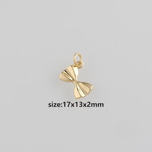 Peut inclure: Un charm doré en forme de nœud papillon. Il comporte une boucle pour l'attache. Le texte "size: 17x13x2mm" est visible. Le charm mesure environ 1,7 x 1,3 x 0,2 cm.