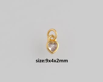 Puede incluir: Un dije dorado en forma de corazón con una piedra transparente en forma de corazón en el centro. El dije tiene un lazo en la parte superior para sujetarlo. El texto "size:9x4x2mm" está debajo.