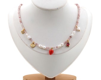 May include: A delicate pink and white beaded necklace with gold heart charms and a red heart pendant. The necklace is displayed on a white mannequin bust.