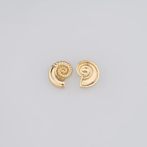 May include: A pair of gold-toned earrings shaped like seashells. The earrings are small and delicate, with a spiral design.