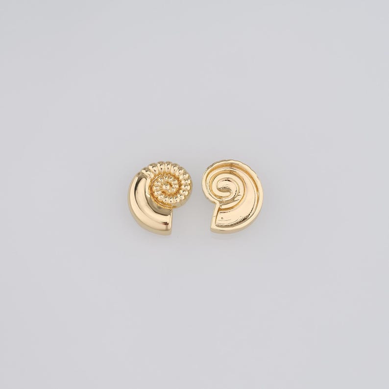 May include: A pair of gold-toned earrings shaped like seashells. The earrings are small and delicate, with a spiral design.