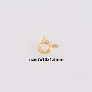 May include: A gold-colored spring ring clasp for jewelry making. The clasp is round with a small lever and a loop for attaching to a chain or other jewelry component. The text "size: 7x10x1.5mm" is below the clasp.