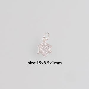 Könnte beinhalten: Ein kleiner, silberfarbener Ahornblatt-Anhänger mit detailliertem Blattdesign. Der Anhänger misst 1,5 cm x 0,85 cm x 1 mm und hat eine kleine Schlaufe zum Befestigen. Der Text "size:15x8.5x1mm" befindet sich darunter.