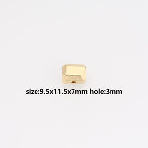 Puede incluir: Una cuenta geométrica dorada con un agujero. La cuenta mide 9,5x11,5x7mm, con un agujero de 3mm. El texto "size:9.5x11.5x7mm hole:3mm" está impreso debajo.