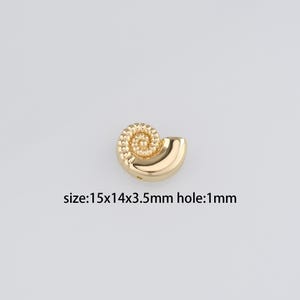 May include: Gold-colored seashell charm with a spiral design. The charm measures 1.5 x 1.4 x 0.35 inches and has a 1 mm hole.