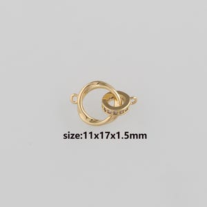 May include: Gold-colored jewelry connector with two interlocking rings. One ring is plain, while the other is adorned with small, clear stones. The text "size:11x17x1.5mm" is displayed below the connector.