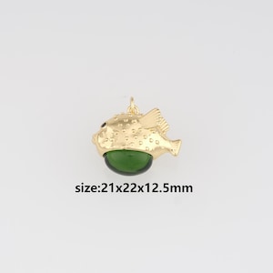 May include: A gold-coloured fish pendant with a green belly. The pendant has a textured surface and a small loop at the top for hanging. The text "size: 21x22x12.5mm" is below the pendant.