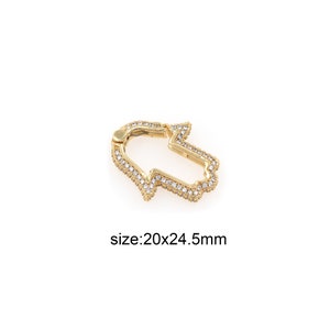 May include: A gold-colored Hamsa hand-shaped charm with clear, sparkling stones. The charm measures 20mm x 24.5mm. The Hamsa hand is a symbol of protection and good fortune, often used in jewelry and decorative items.