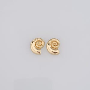 May include: A pair of gold-tone earrings shaped like seashells with a spiral design.
