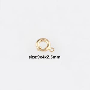 Op de afbeelding: Een goudkleurige veering sluiting met een cirkelvormig ontwerp en een kleine lus. De tekst "size:9x4x2.5mm" is eronder afgedrukt. Deze sluiting wordt gebruikt voor kettingen en armbanden.