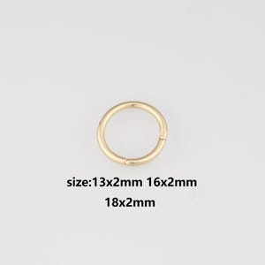 Puede incluir: Un cierre circular dorado con una abertura articulada. La imagen incluye texto que indica los tamaños disponibles: 13x2mm, 16x2mm y 18x2mm. El cierre está sobre un fondo liso y claro.