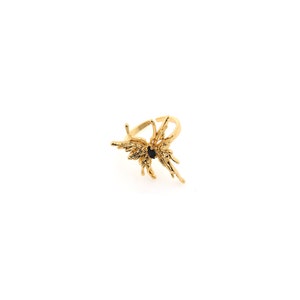 May include: A gold-colored ring with an abstract butterfly design. The ring features a central black stone and intricate, textured wings. The ring is set against a white background, highlighting its details.