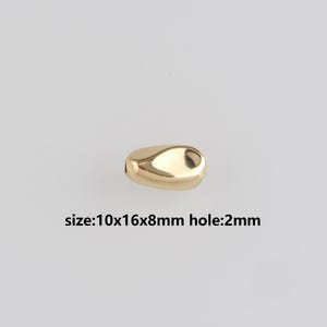 Pode incluir: Uma conta dourada em forma de gota com um furo de 2 mm. A conta mede 1 cm x 1,6 cm x 0,8 cm. A conta tem uma superfície lisa e polida. O texto na imagem diz: size:10x16x8mm hole:2mm.