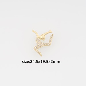 May include: A gold-toned charm in the shape of a dancer, embellished with clear, sparkling stones. The dancer is in a dynamic pose, with outstretched arms and a raised leg. The text "size:24.5x19.5x2mm" is below the charm.