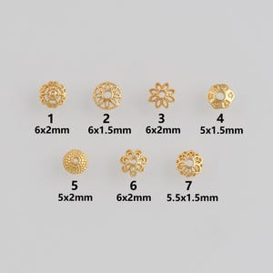 May include: Seven gold-colored metal bead caps in various floral and geometric designs. Each bead cap is labeled with its size in millimeters. The beads are arranged in two rows on a light gray background.