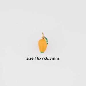 May include: A gold-colored mango charm with orange enamel and a green leaf. The charm measures 16mm x 7mm x 6.5mm. The mango has a gold loop at the top for attaching to a necklace or bracelet. The charm is set against a white background.