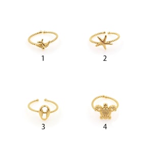 May include: Four gold-toned adjustable rings with different sea-life designs. The rings feature a dolphin, a starfish, a seashell, and a turtle.