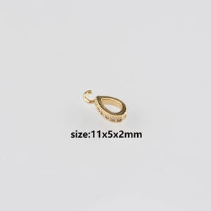 May include: A gold-coloured teardrop-shaped charm with a small loop at the top. The charm is embellished with small, clear stones. The text "size: 11x5x2mm" is below the charm. Measurements: 1.1cm x 0.5cm x 0.2cm.