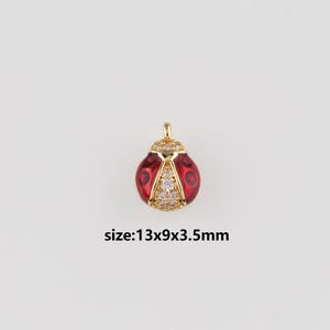 Puede incluir: Un colgante de mariquita dorado con esmalte rojo y detalles de cristal transparente. El colgante mide 13x9x3,5mm. El cuerpo de la mariquita es rojo con lunares negros, y la cabeza está adornada con cristales.