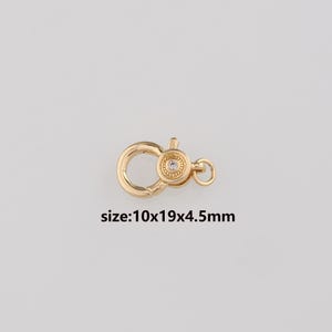 Puede incluir: Un cierre de langosta dorado con una pequeña gema transparente en el centro. El cierre mide aproximadamente 10 mm de ancho, 19 mm de largo y 4,5 mm de grosor. El texto "size:10x19x4.5mm" está debajo.