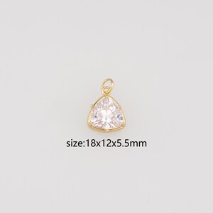 Puede incluir: Un colgante de tono dorado con una piedra preciosa triangular transparente y facetada en un marco de metal con una pequeña anilla en la parte superior. El texto size:18x12x5.5mm aparece debajo, indicando sus dimensiones.