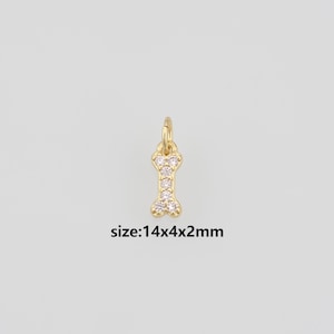 May include: A gold-toned dog bone charm featuring five embedded clear stones and a small jump ring at the top. The charm is labeled with the text size:14x4x2mm, indicating its physical dimensions in millimeters for clear identification.