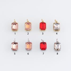 May include: Eight square-shaped pendants with different coloured glass stones. The pendants are numbered 1 through 8. The stones are clear, pink, red, and light pink.