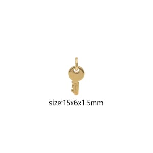 May include: A gold-colored key charm pendant measuring 1.5 cm in length, 0.6 cm in width, and 0.15 cm in thickness. The key charm has a simple design with a round head and a straight shaft.