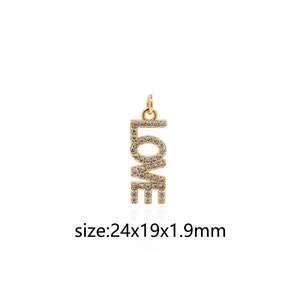 May include: Gold pendant charm with the word "LOVE" spelled out in block letters. Each letter is covered in small, clear cubic zirconia stones. The pendant measures 24 x 19 x 1.9 mm.