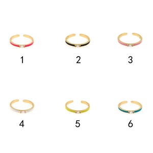 May include: Six gold rings with a single clear stone and a colored enamel band. The rings are numbered 1 through 6. The colors are pink, black, light pink, white, yellow, and teal.