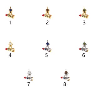 May include: Eight silver and gold astronaut charms with different colored gemstones. Each charm features an astronaut riding a rocket with red, white, and blue accents.